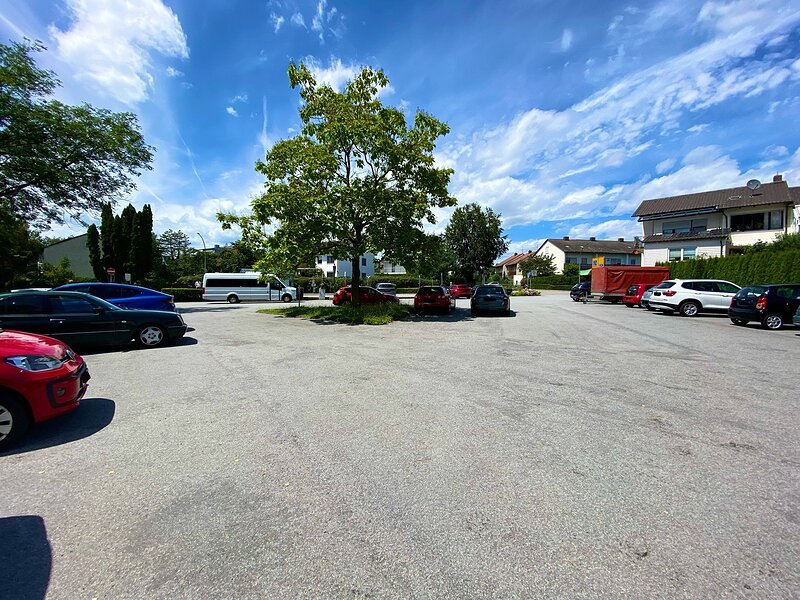 Parkplatz mit mehreren geparkten Autos und einem Baum in der Mitte unter blauem Himmel mit Wolken