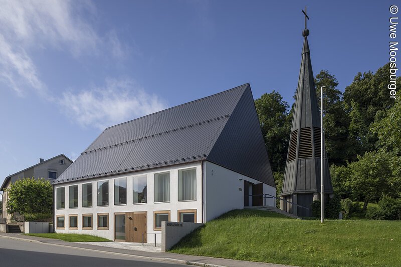 Markt Bad Abbach Kreuzkirche Evangelisch-Lutherische Kirchengemeinde Bad Abbach Kirchengebäude mit spitzem Dach und separatem Glockenturm mit Kreuz umgeben von Bäumen und Rasenfläche.