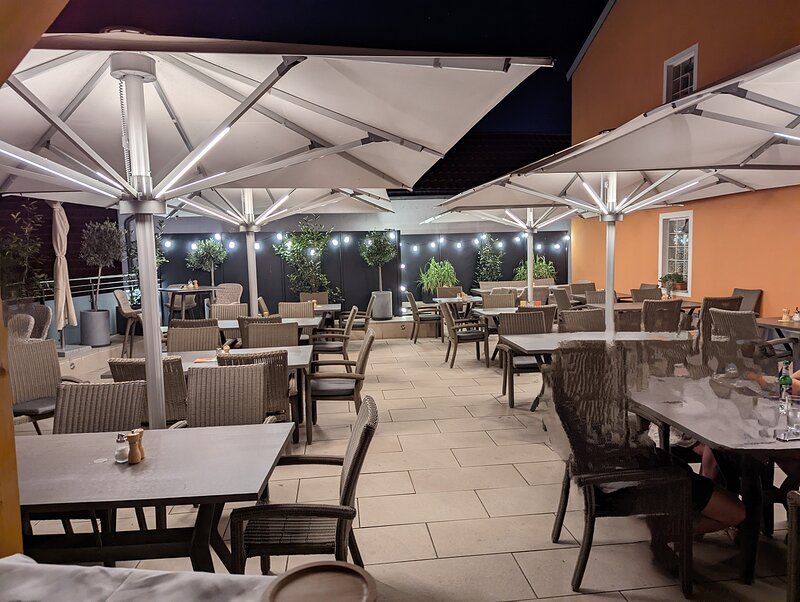 Dachterrasse Fischerwirt am Abend Außenbereich eines Restaurants mit Tischen, Stühlen, großen Sonnenschirmen und Beleuchtung bei Nacht.