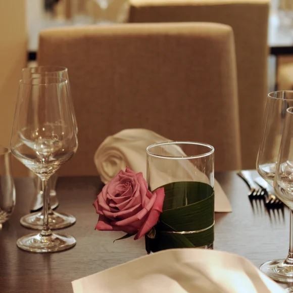 Gedeckter Tisch mit Weingläsern, Serviette und Glas mit rosa Rose in einem Restaurant.