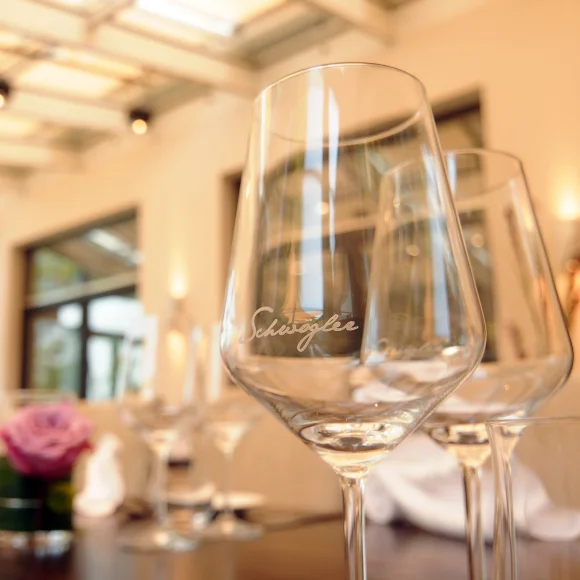 Weingläser auf einem gedeckten Tisch in einem hellen Raum mit großen Fenstern und Blumenarrangement.