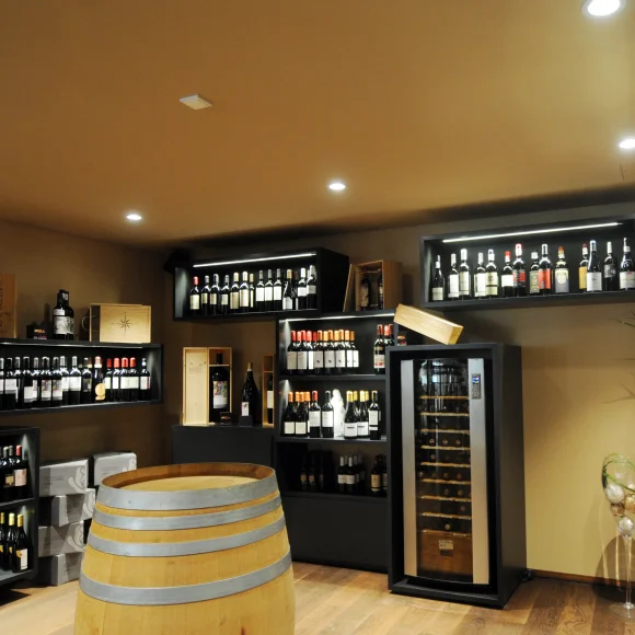 Weinkeller mit Regalen voller Weinflaschen, einem Weinkühlschrank und einem Holzfass in der Mitte.