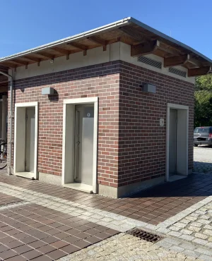 Gebäude mit drei Türen, Parkplatz mit Behindertenparkplatzschild und mehreren Autos im Hintergrund.