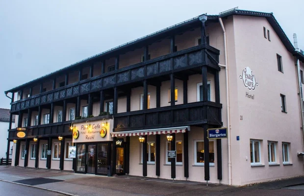 Fassade eines Hotels mit Café, Restaurant und Biergarten, beleuchtete Eingänge und Balkone aus Holz.
