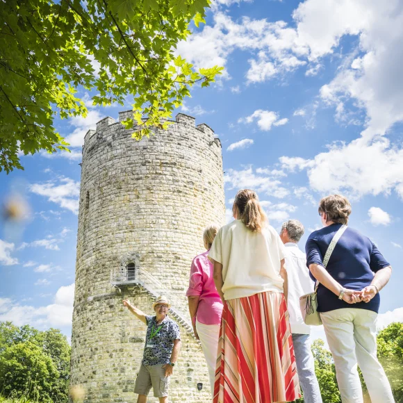 Gruppe von Menschen steht vor einem alten Steinturm, ein Mann zeigt auf den Turm.
