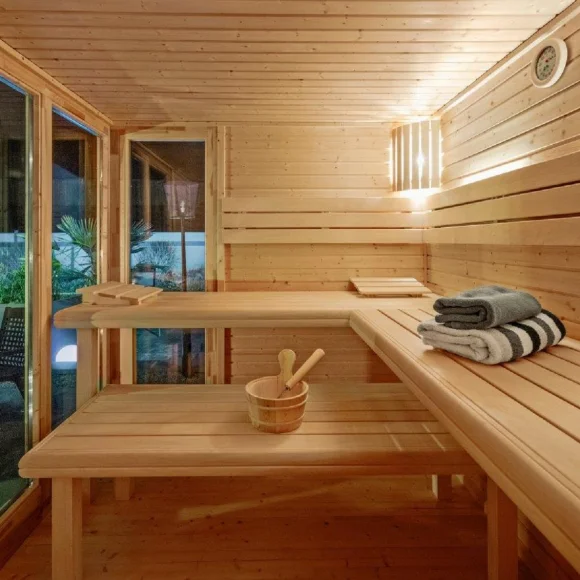 Innenraum einer Holzsauna mit Bänken, einem Eimer und Handtüchern, Fenster mit Blick auf Garten.