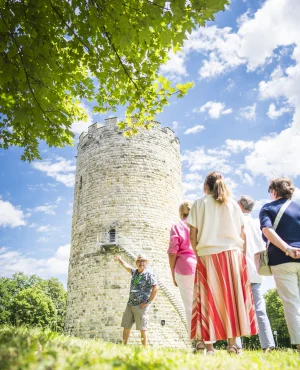Gruppe von Menschen vor einem runden Steinturm, ein Mann zeigt auf den Turm.